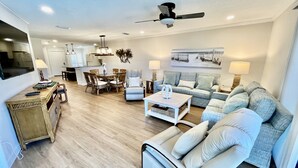 A spacious living room with a sofa, coffee table, and TV. There is a dining area with chairs and a table. The room has wooden flooring and ceiling fans. - FREE ACTIVITIES & A gorgeous ocean view unit ready for your enjoyment. (Saint Augustine)