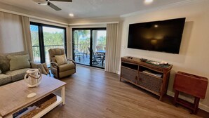 A spacious living room with a ceiling fan, a flat-screen TV, a sofa, a coffee table, and a sliding glass door leading to an outdoor patio. - FREE ACTIVITIES & A gorgeous ocean view unit ready for your enjoyment. (Saint Augustine)