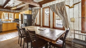 A rustic kitchen with wooden cabinets, a large wooden table, and a refrigerator.