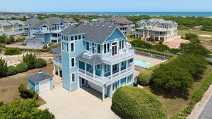 Ein großes, mehrstöckiges Haus mit Schwimmbad, umgeben von anderen Häusern und Blick auf den Strand.