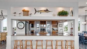 Eine moderne Küche mit einer zentralen Kochinsel, Holzbarhocker und Wandkunst, darunter ein Fisch und Vögel.