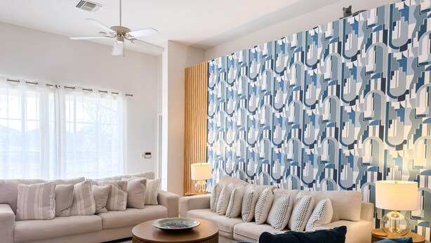 Ein modernes Wohnzimmer mit einem beigen Sofa, einem blauen Sessel und einer Wand mit Muster.