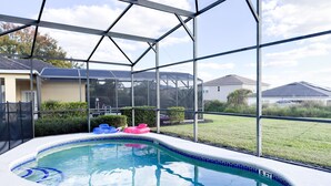 Ein Schwimmbad mit Glasveranda, umgeben von einem Rasen und Häusern.