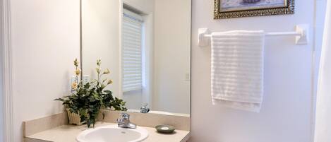 A bathroom with a sink, mirror, toilet, towel rack, and a framed picture on the wall.