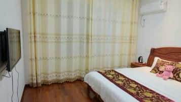 A bedroom with a wooden floor, a bed with a white and red bedspread, a pink teddy bear on the bed, and a television mounted on the wall.
