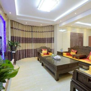 A modern living room with a large dark wooden coffee table, two sofas with colorful cushions, and a large window with striped curtains.