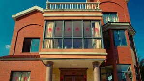 Un edificio de dos pisos con entrada central, ventanas grandes y un balcón.