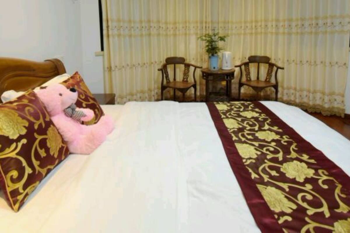 A hotel room with a bed, a teddy bear, a small table with chairs, and a potted plant.