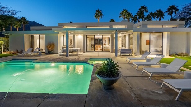 A modern house with a swimming pool, outdoor seating, and a well-lit patio area.