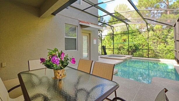 Une terrasse fermée par des baies vitrées, avec une piscine, une table et des chaises, et un vase rempli de fleurs.