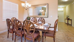 Un coin repas comprenant une grande table rectangulaire, six chaises en bois, un lustre et un miroir au mur.