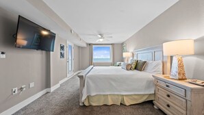 Un dormitorio con cama, televisión montada en la pared, ventilador de techo y ventana con vistas.
