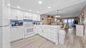 Una cocina moderna con armarios blancos, una isla grande y vista al área de estar.