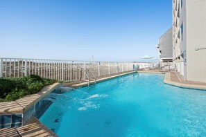 A pool with a white fence, a lifeguard chair, and a building with a flag.