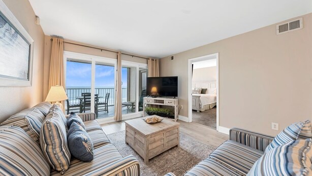 Una sala de estar moderna con un conjunto de sofá, una mesa de centro y un televisor. Hay un balcón con vistas al cielo.