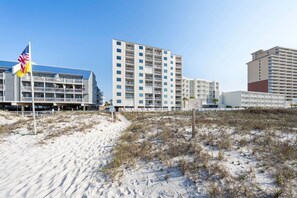 A beachfront hotel with multiple-story buildings, a sandy beach, and a flag.