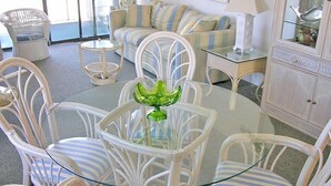 A dining area with a round glass table surrounded by white wicker chairs with blue stripes. - Even Keel 404-Oceanfront 75th St, Elev, W/D, AC (Ocean City)