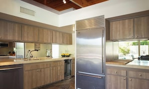 A modern kitchen with wooden cabinets, a stainless steel refrigerator, and a dishwasher. - Mid-Century Home with Theater and Spa (Palm Springs)