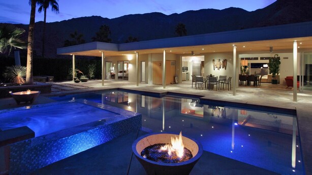 Una casa moderna con piscina, mobiliario exterior y una chimenea.