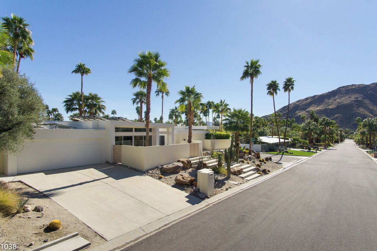 A modern residential street with palm trees, a mountain in the background, and a clear sky.