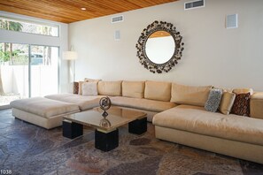 A modern living room with a sectional sofa, a coffee table, and a decorative mirror. - Mid-Century Home with Theater and Spa (Palm Springs)