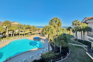 A resort with a swimming pool, palm trees, and a view of the ocean.
