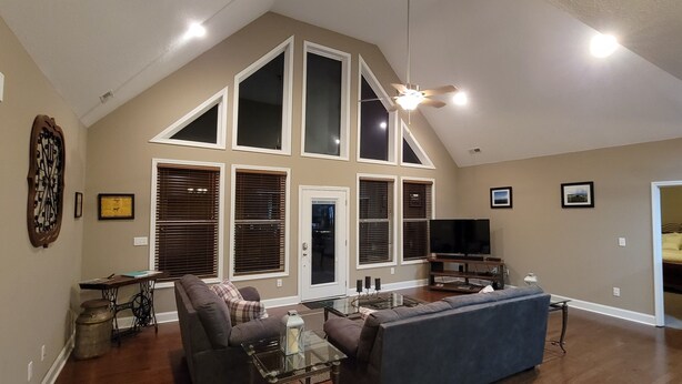 Un salón amplio con techo alto, ventanas grandes, un televisor y un sofá.