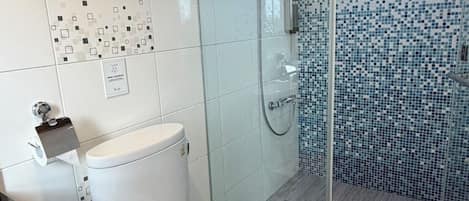 Un baño moderno con inodoro, ducha con mampara de vidrio y pared de azulejos con diseño tipo mosaico.