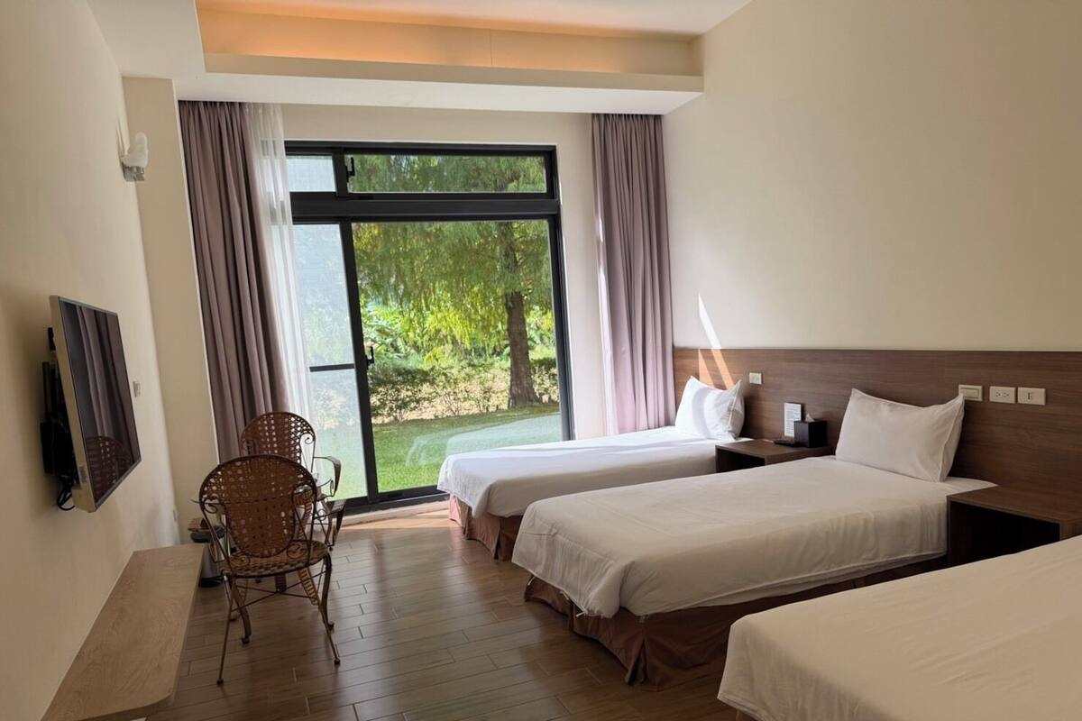 Habitación de hotel con dos camas, una silla, un televisor y un ventanal con cortinas.