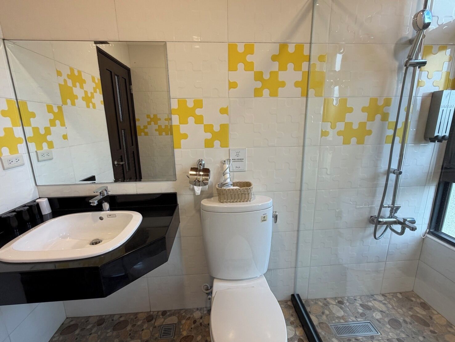 Un baño con un lavamanos blanco, encimera negra y un inodoro. Las paredes están cubiertas de azulejos con un diseño amarillo y blanco.