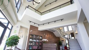 En rummelig lobby med en central trappe, træpaneler og en receptionsdisk med en udstilling af genstande.
