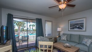 A living room with a pool view, a ceiling fan, a sofa, a coffee table, and a TV.