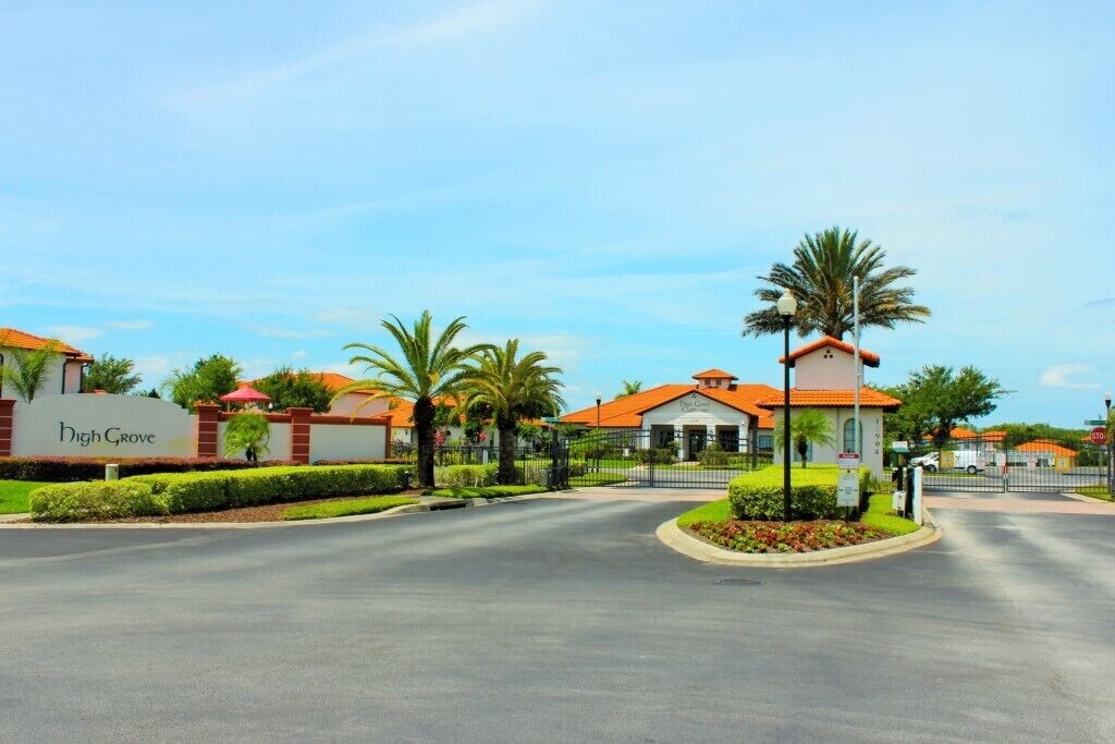 Un complejo residencial cerrado con una avenida central, palmeras y un edificio con el cartel 'High Grove'.