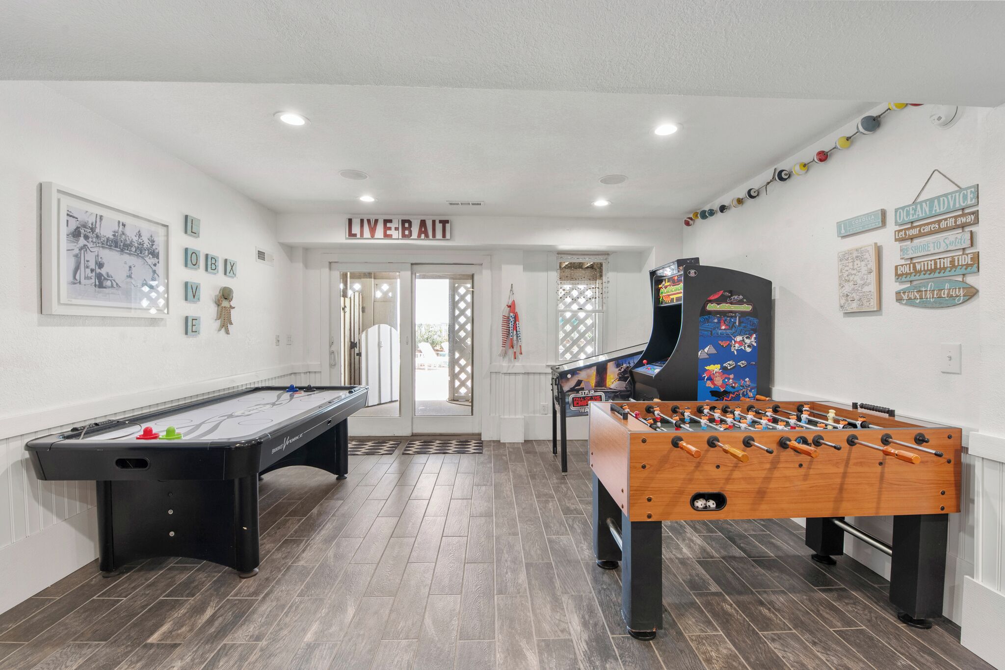 A pool table, foosball table, and arcade games in a room with white walls and a door labeled 'LIVE-BAIT'.