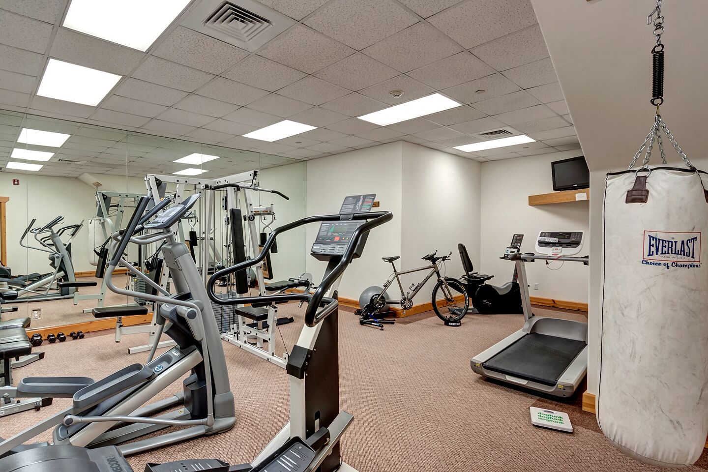 Une salle de sport équipée de divers appareils, notamment des tapis de course, un vélo d’appartement et un sac de frappe.