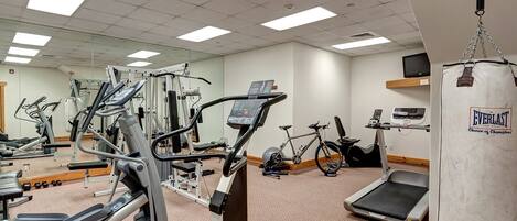 Une salle de sport équipée de divers appareils, notamment des tapis de course, un vélo d’appartement et un sac de frappe.