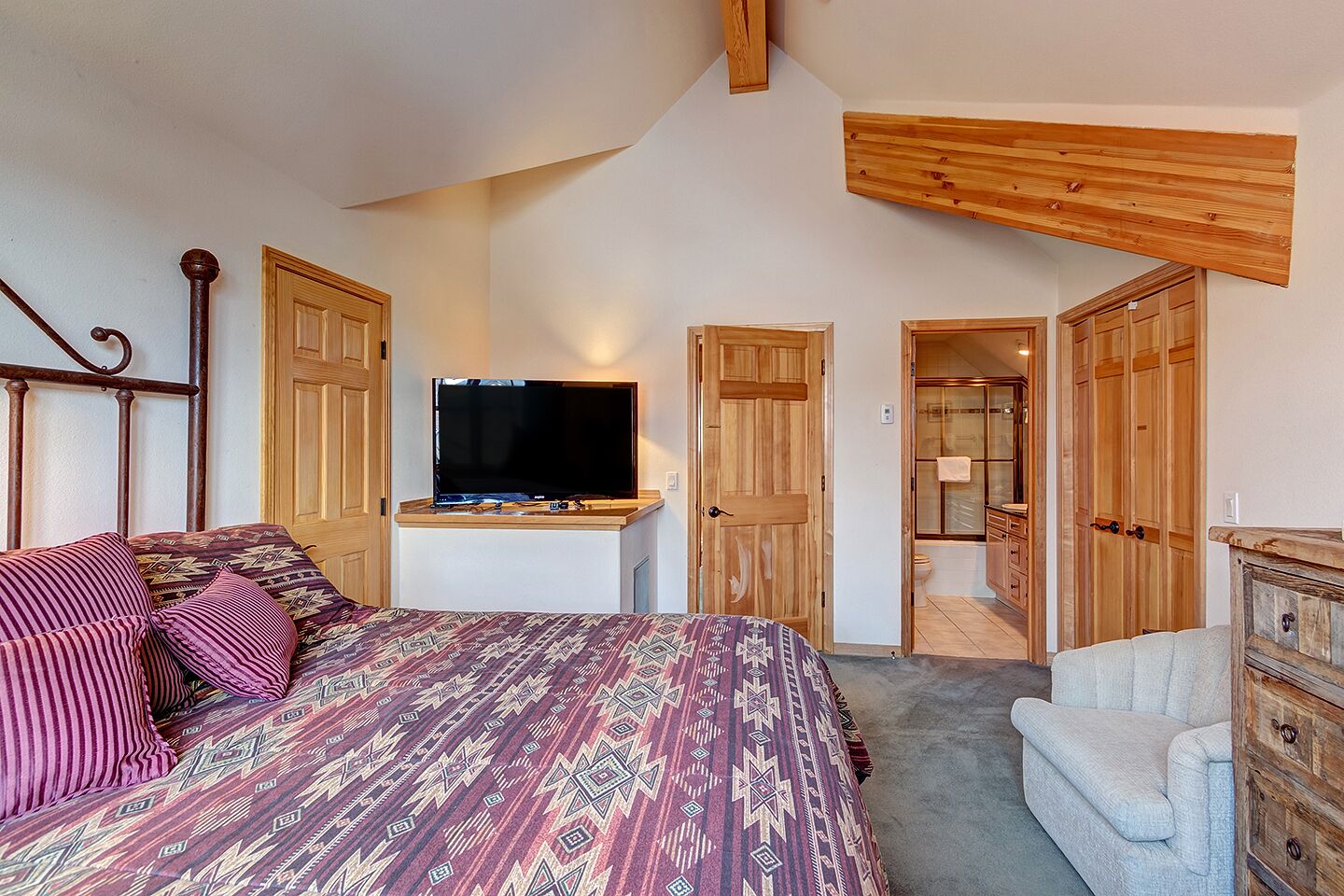 Une chambre à coucher comprenant un lit, un téléviseur, une commode et une porte en bois donnant sur une salle de bain.