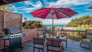 Une terrasse extérieure équip ée d’un barbecue, d’une table, de chaises et d’un grand parasol.