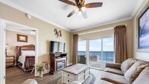 A spacious living room with a large sofa, a coffee table, and a TV. There is a balcony with a view of the ocean. - Gulf Shores Condo with Gulf Views | Lazy River, Pools, and Hot Tub | Sleeps 6 (Gulf Shores)