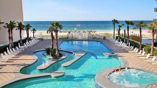 A pool area with multiple swimming sections, a hot tub, and a view of the beach. - Gulf Shores Condo with Gulf Views | Lazy River, Pools, and Hot Tub | Sleeps 6 (Gulf Shores)