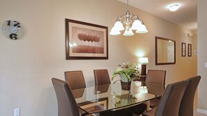A dining area with a glass table, brown chairs, a chandelier, a framed picture, and a clock on the wall. - Newly Renovated | Walk to Clubhouse | South-Facing Pool Near Disney (Kissimmee)