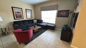 A living room with a sofa, a red chair, a coffee table, and a TV stand. - Newly Renovated | Walk to Clubhouse | South-Facing Pool Near Disney (Kissimmee)