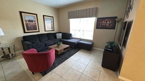 A living room with a sofa, a red chair, a coffee table, and a TV stand. - Newly Renovated | Walk to Clubhouse | South-Facing Pool Near Disney (Kissimmee)