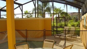 A covered outdoor seating area with tables and chairs, a glass enclosure, and a view of greenery. - Newly Renovated | Walk to Clubhouse | South-Facing Pool Near Disney (Kissimmee)