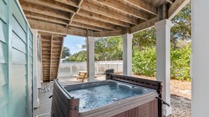 Un bain à remous sous une pergola en bois, avec vue sur une clôture blanche et une végétation luxuriante.