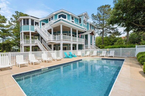 Une maison à deux étages avec une piscine, des balustrades blanches et plusieurs niveaux dotés de balcons.