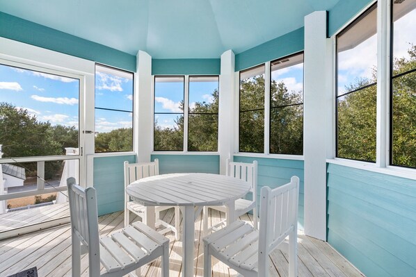 A covered outdoor area with a white table and chairs, large windows, and a view of trees and a building. - Bermuda Banks: Private Pool, Spa, Pet-friendly (Corolla)