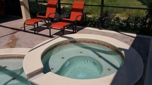A hot tub with a tiled edge, surrounded by a stone patio. There are two red lounge chairs and a small table. - Luxurious Home with Private Pool Upstairs  Games Room. 928 (Davenport)