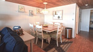 A dining area with a wooden ceiling, white walls, and a chandelier. There is a table with chairs, a trash can, and a small house decoration on the table. - Cozy 1 Bedroom Oceanfront Condo with Free WiFi, Beach Decor, an Outdoor Pool, and a Breathtaking View Located Midtown and Steps from the Beach! (Ocean City)