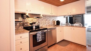 A modern kitchen with white cabinets, stainless steel appliances, a tiled backsplash, and wooden flooring. - Cozy 1 Bedroom Oceanfront Condo with Free WiFi, Beach Decor, an Outdoor Pool, and a Breathtaking View Located Midtown and Steps from the Beach! (Ocean City)